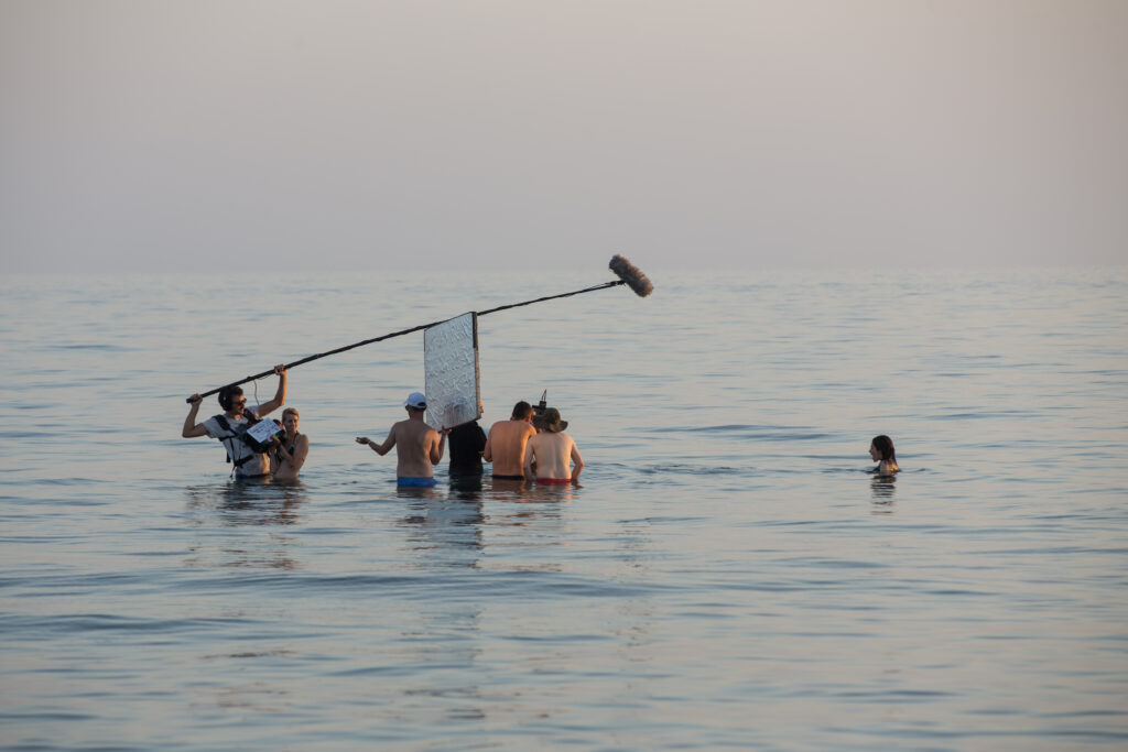 Una foto del dietro le quinte del film "Giulia" di Ciro De Caro: la troupe, tra cui spicca un fonico con un microfono ad asta molto lungo, è immersa nell'acqua per riprendere una scena dove un'attrice fa un bagno in mare.